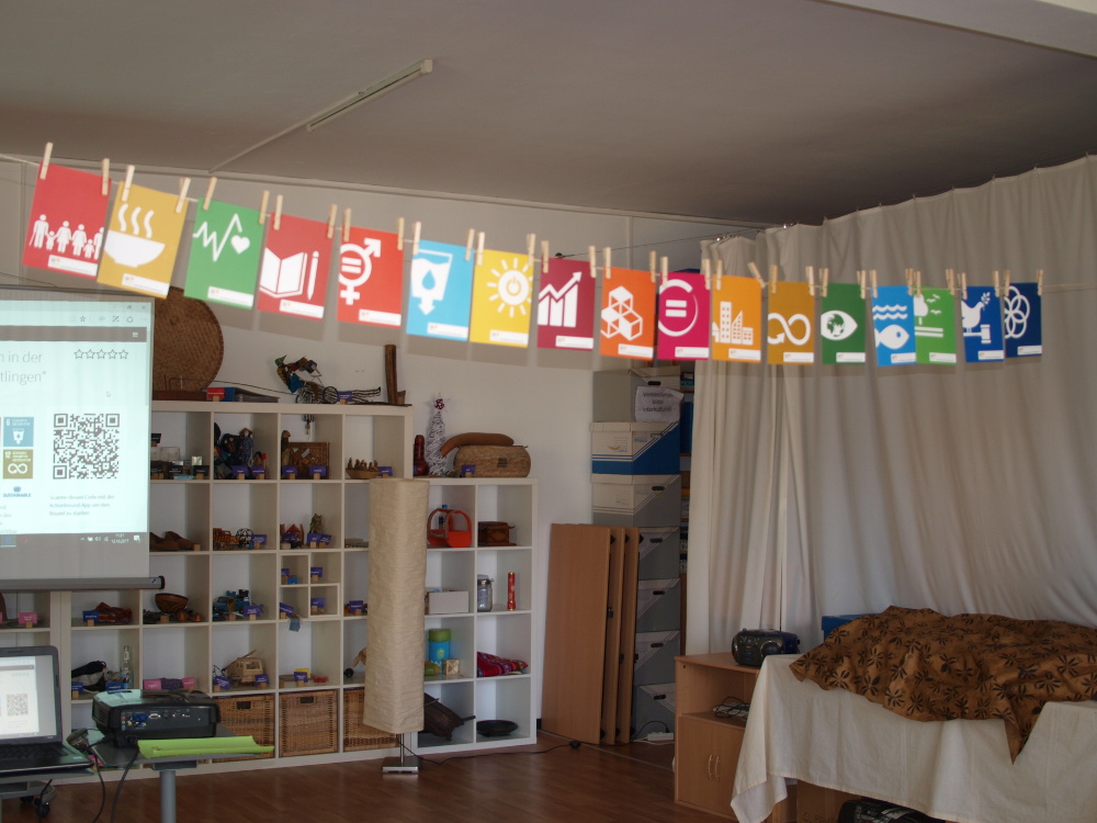 Einblick in das Globale Klassenzimmer Reutlingen - Gegenstände in Regalen, eine Leinwand, SDG-Karten an einer Wäscheleine. Quelle: epiz.de