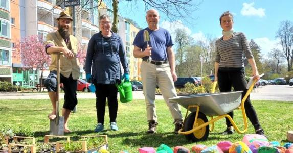 Vier Personen mit Gartengeräten vor einer Wohnsiedlung.