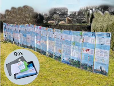 Hellblau-weiß gestaltete Plakate nebeneinander auf einer Wiese bei Sonnenschein. SDG Ausstellung "17 Ziele für eine bessere Welt".