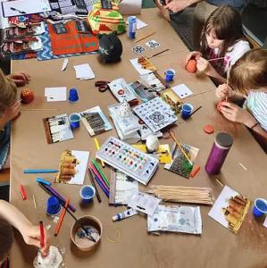 Kinder sitzen um Tisch mit Mal- und Bastelutensilien. Workshop-Szene aus der Grundschule zu nachhaltigem Bauen. Quelle: we-building.org 