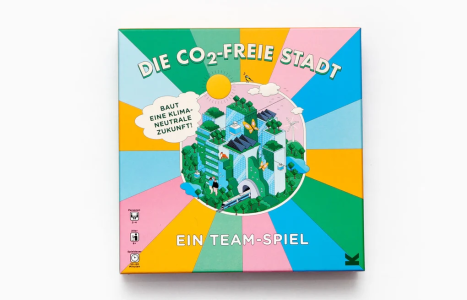 Spielschachtel „Die CO₂-freie Stadt – Ein Team-Spiel": Buntes Cover mit illustrierter grüner Stadt der Zukunft, Solarpanelen und Windrädern. Für 2–4 Personen ab 8 Jahren, Spieldauer 30–60 Minuten.