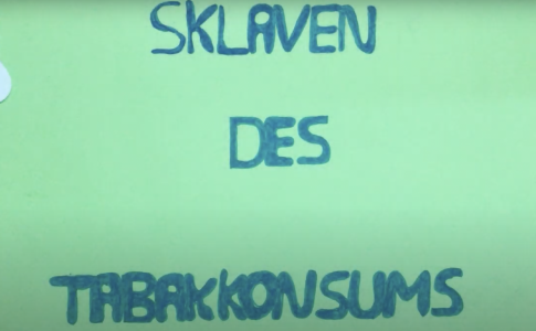 Blaue Schrift “Sklaven des Tabakkonsums“ auf grünem Hintergrund.