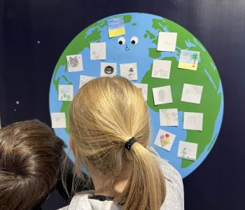 Kinder schauen auf eine Weltkarte, die bemalte Post-It-Zettel trägt.