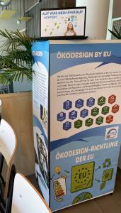 Ausstellungsstand mit Banner zur „Ökodesign-Richtlinie der EU" (Kriterien wie Recycling, Reparierbarkeit, Energieeffizienz) und Laptop mit „Auf was beim Einkauf achten?" im Hintergrund.