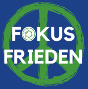 ChatGPT:  Das Bild zeigt den Text „FOKUS FRIEDEN“ in weißen Großbuchstaben auf blauem Hintergrund. Der Buchstabe „O“ in „FOKUS“ ist durch ein Kameraobjektiv-Symbol ersetzt. Im Hintergrund ist ein grün gezeichnetes Peace-Zeichen zu sehen.