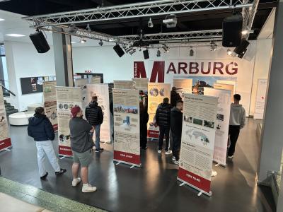 bitte dasselbe11:52Claude hat geantwortet: Schülerinnen und Schüler betrachten eine Wanderausstellung in der Aula der Schulen Marburg.Schülerinnen und Schüler betrachten eine Wanderausstellung in der Aula der Schulen Marburg. Roll-up-Banner zu Themen wie „Fokus Lithium", „Fokus Palmöl" und „Planetare Grenzen" sind aufgestellt.