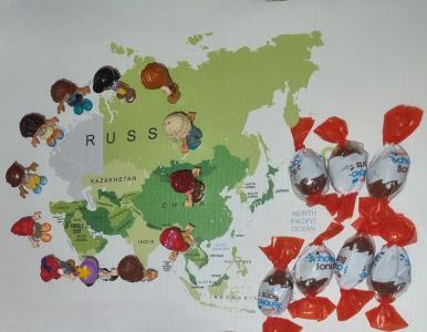 Spielfiguren stehen im Kreis auf einer Weltkarte, an der Seite liegen einige Schokopralinen. Bild aus dem Verteilungsspiel. Quelle: Netzwerk Steuergerechtigkeit