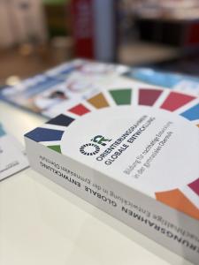 bitte dasselbeNahaufnahme der gedruckten Publikation „Orientierungsrahmen Globale Entwicklung – Bildung für nachhaltige Entwicklung in der gymnasialen Oberstufe", mit dem farbigen SDG-Rad auf dem Cover, auf einem Tisch liegend.