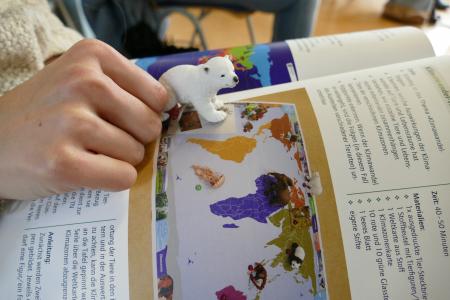 Auf einem aufgeklappten Heft läuft ein Spielzeugeisbär.