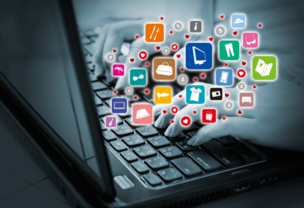 Zu sehen ist in Grautönen, wie jemand auf einer Laptop-Tastatur tippt. Aus dem Bildschirm schweben bunte Symbole mit Einkaufs-, Kleidungs- und Technik-Icons hervor. 