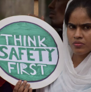 Eine wütend schauende Frau hält ein Schild mit der Aufschrift "Think safety first".