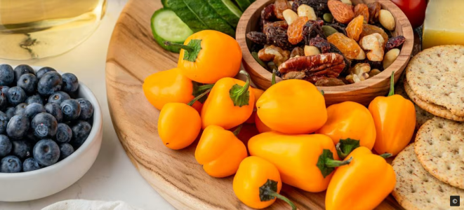 Ein Teller mit gelben Paprika, Blaubeeren, Gurken, Datteln und Nüssen.