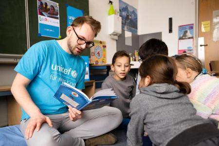 UNICEF Mitarbeiter und Kinder sitzen in einem Kreis und lesen gemeinsam
