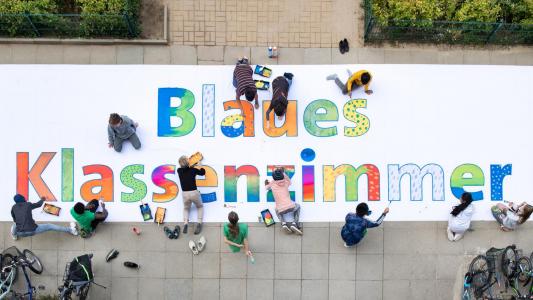 Kinder malen ein riesiges Banner mit der Aufschrift "Blaues Klassenzimmer"