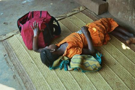 Mädchen liegt auf Teppich mit rotem Schulranzen neben ihr.