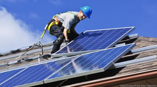 Ein Handwerker montiert Solarzellen auf einem Dach.