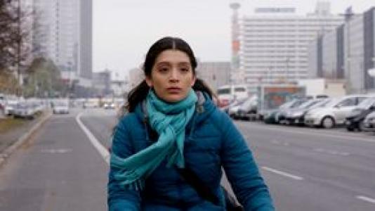 Frau mit blauem Mantel und Schal auf Fahrrad in einer Stadt