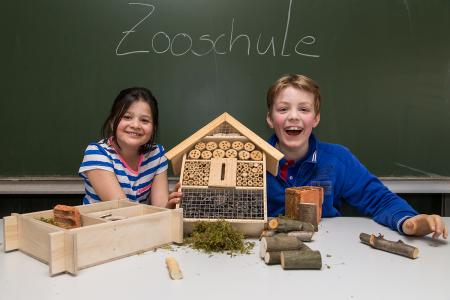 Zwei Kinder zeigen ein Insektenhotel, an der Tafel dahinter steht "Zooschule"