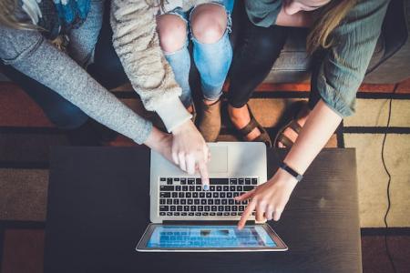 Drei personen sitzen und arbeiten an einem Laptop. Eine Person führt die Hand einer anderen.