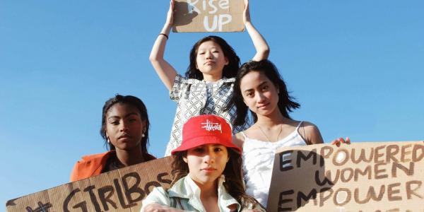 Vier Frauen halten Pappschilder hoch, Aufschrift "We rise up" und "Empower Women"