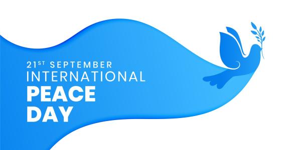 Grafik zum Internationalen Tag des Friedens am 21. September. Eine stilisierte blaue Taube mit einem Olivenzweig fliegt nach rechts. Links steht in weißer Schrift „21st September – International Peace Day“ auf einem blauen, wellenförmigen Hintergrund.