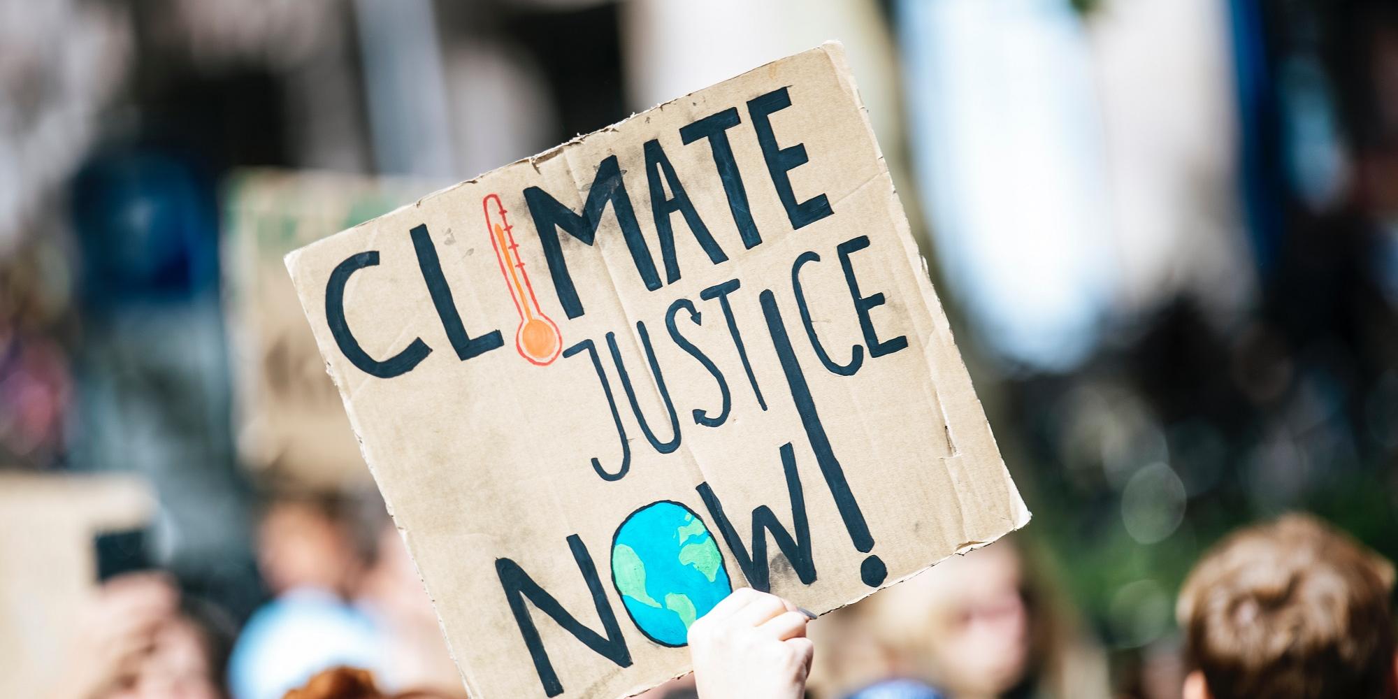 Menschen auf einer Demonstration zum globalen Klimawandel, Schild mit der Aufschrift "Climate Justice Now!"