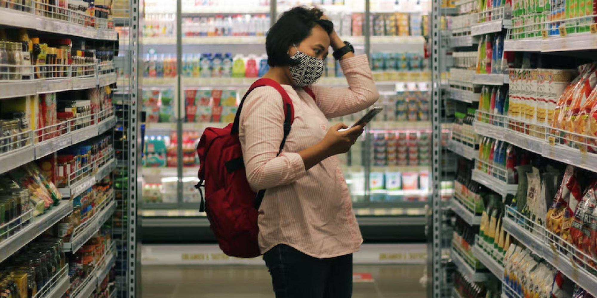 Frau mit Maske und Rucksack vor Supermarktregal. Photo by Viki Mohamad on Unsplash