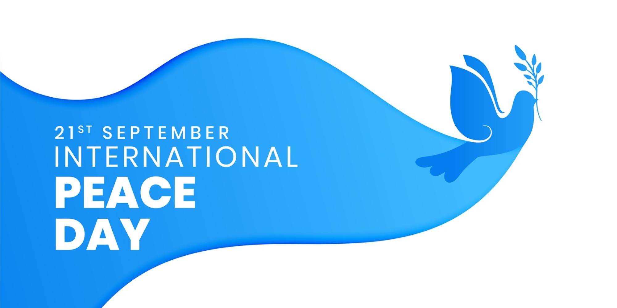 Grafik zum Internationalen Tag des Friedens am 21. September. Eine stilisierte blaue Taube mit einem Olivenzweig fliegt nach rechts. Links steht in weißer Schrift „21st September – International Peace Day“ auf einem blauen, wellenförmigen Hintergrund.